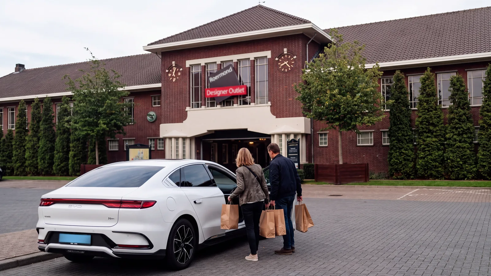Illustratie: entree van Designer Outlet Roermond overdag, een stel met boodschappentassen bij een witte elektrische sedan
