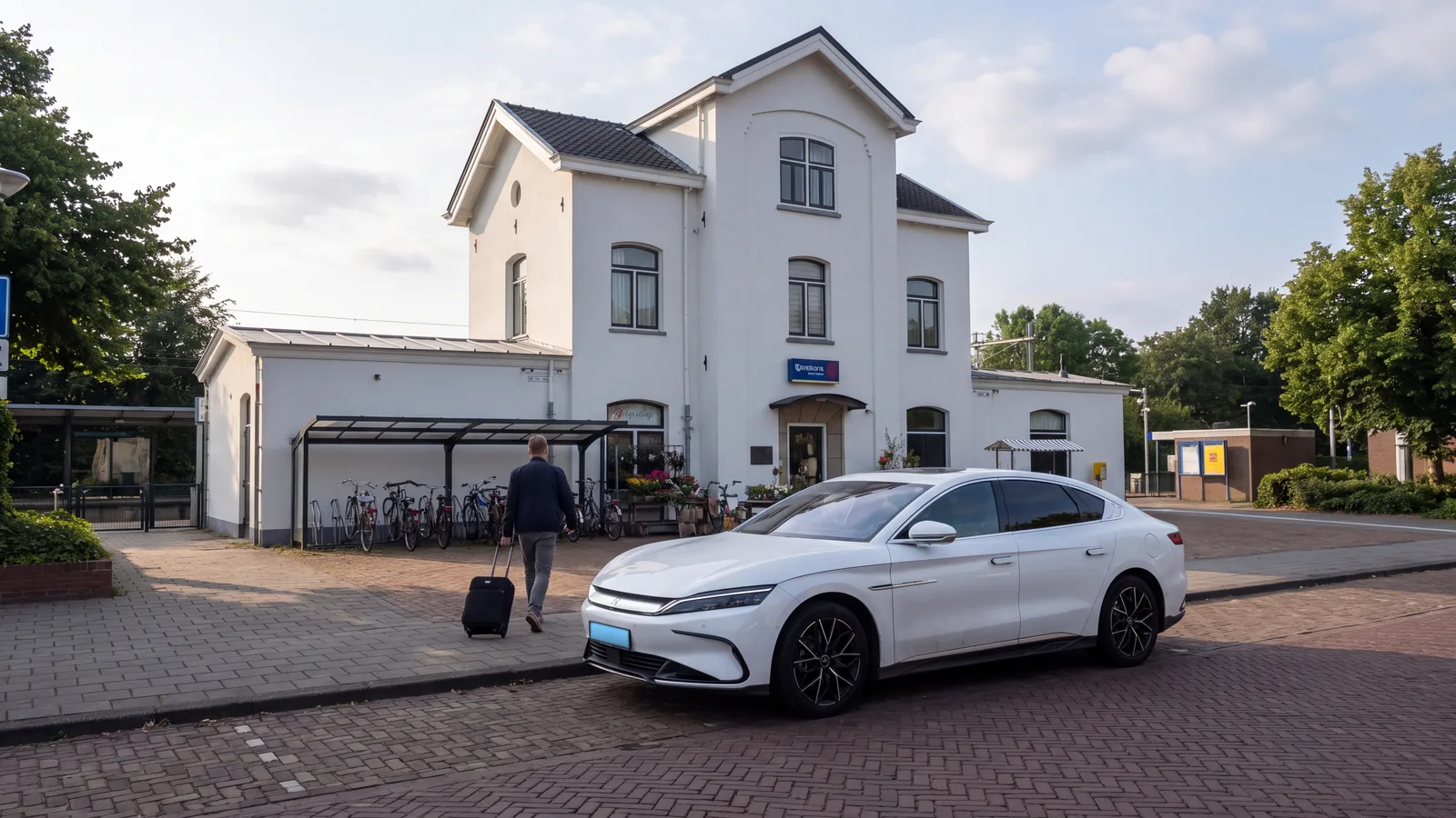 Illustratie: stationsgebouw Echt in de ochtend, een reiziger met koffer en een witte elektrische sedan langs de stoep